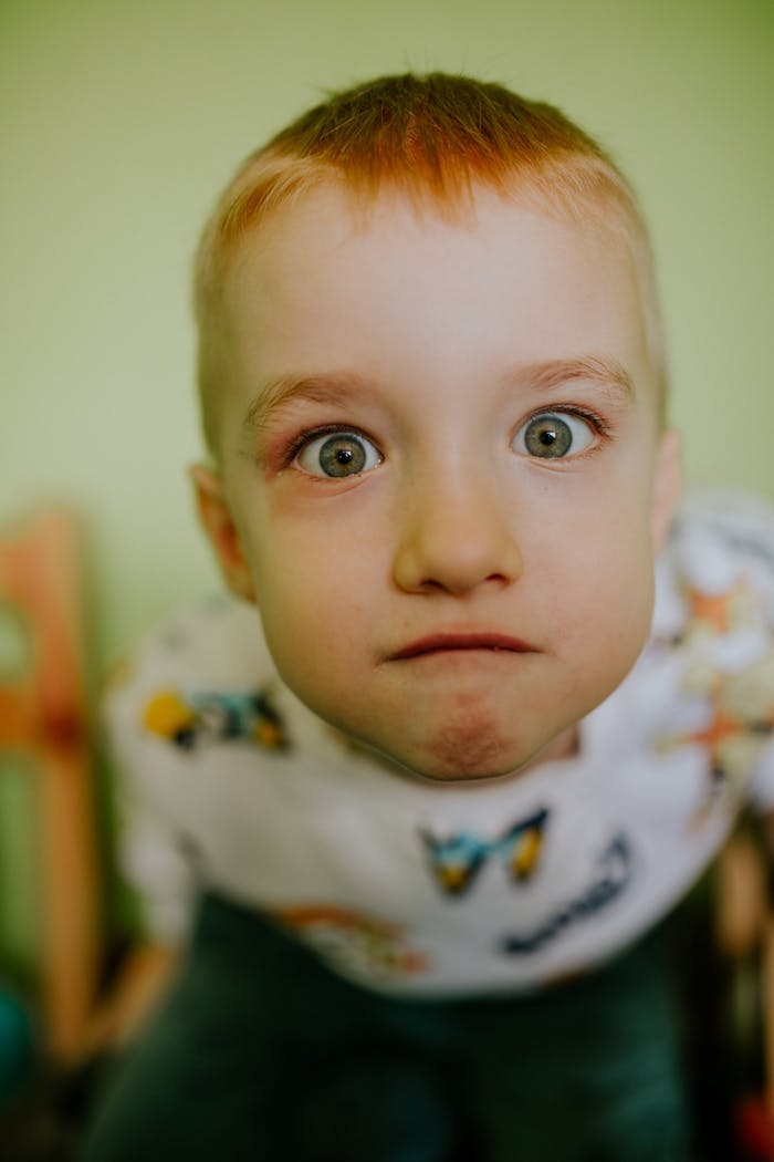 about-us Adorable close-up of a curious red-haired child expressing wonder indoors.