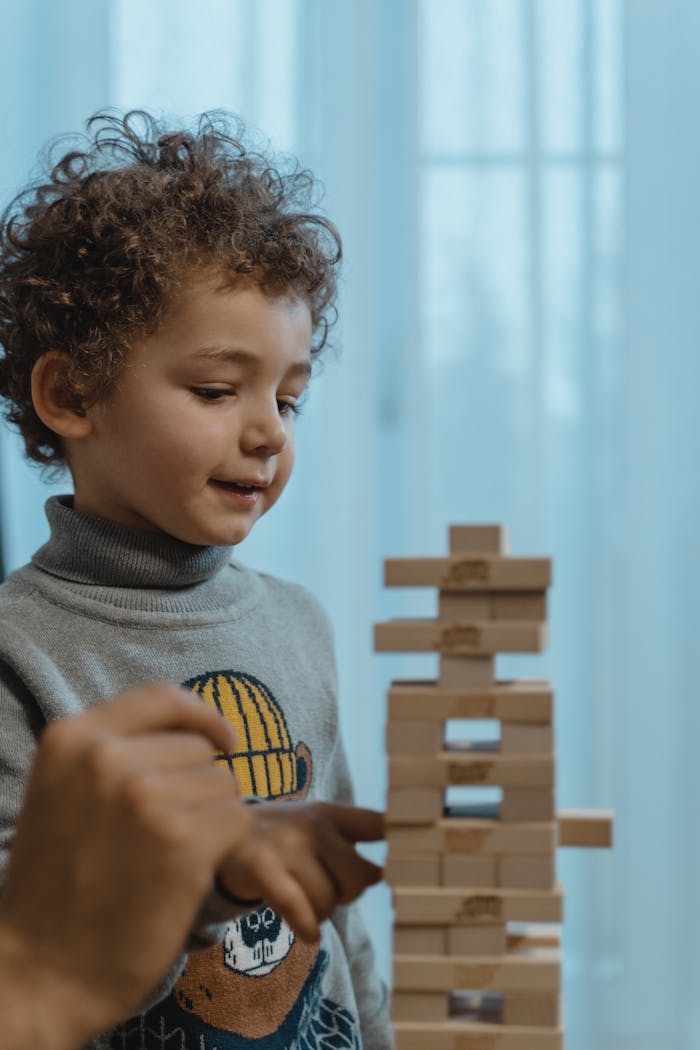 services-01 A young boy plays with wooden blocks, guided by an adult hand indoors.