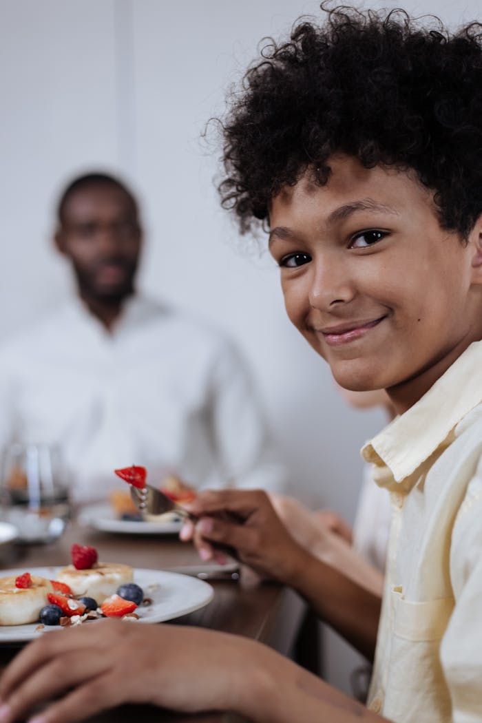 services-02 A joyful moment at the breakfast table with a smiling boy and family enjoying pancakes and berries.